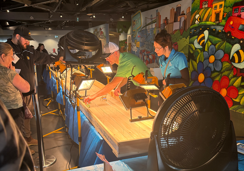 Two judges work to help green energy vehicles down a long wooden track. Spectators look on.